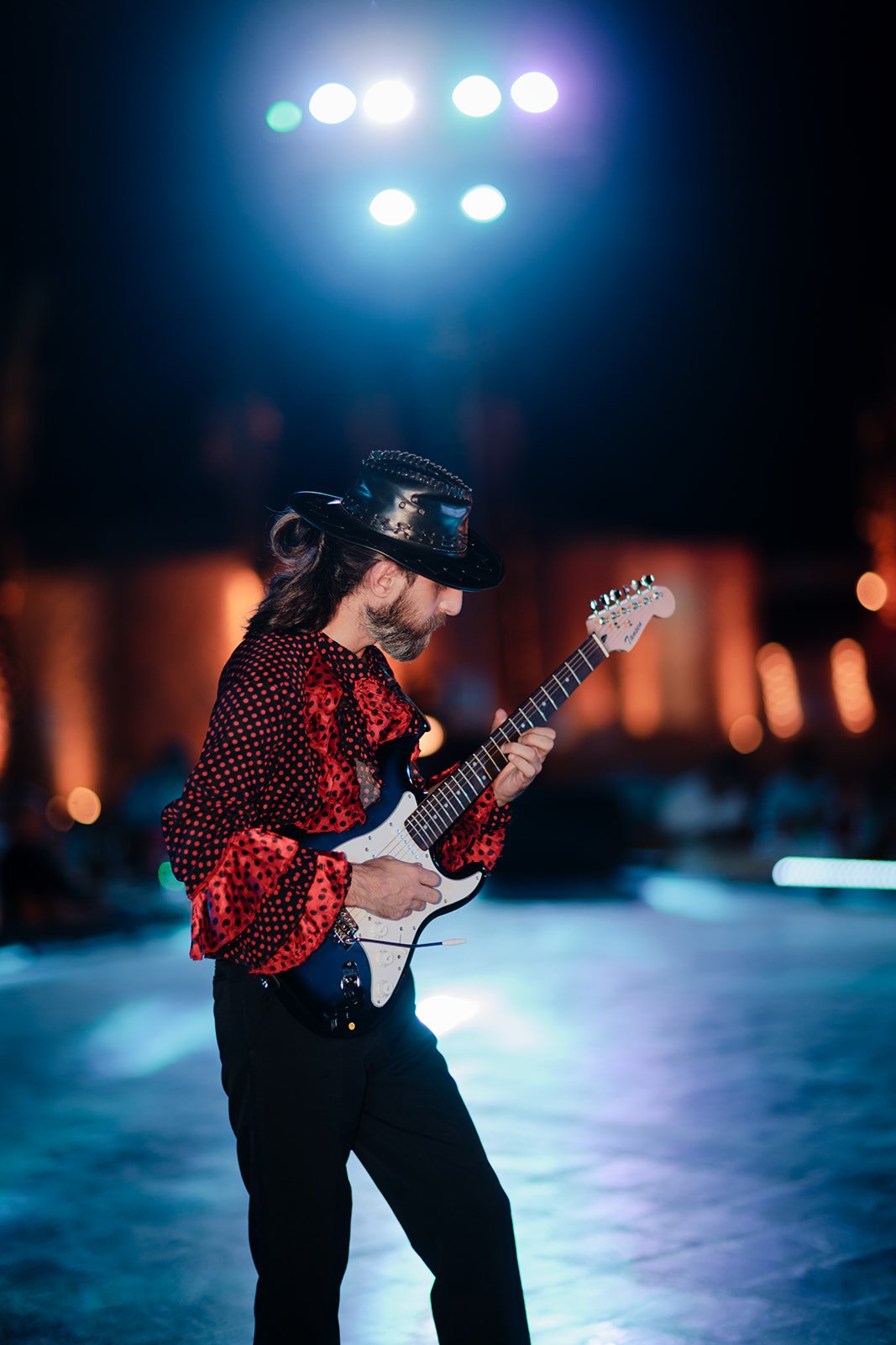An event photograph of a man with a red outfit playing a guitar with blue lights shinning all around him