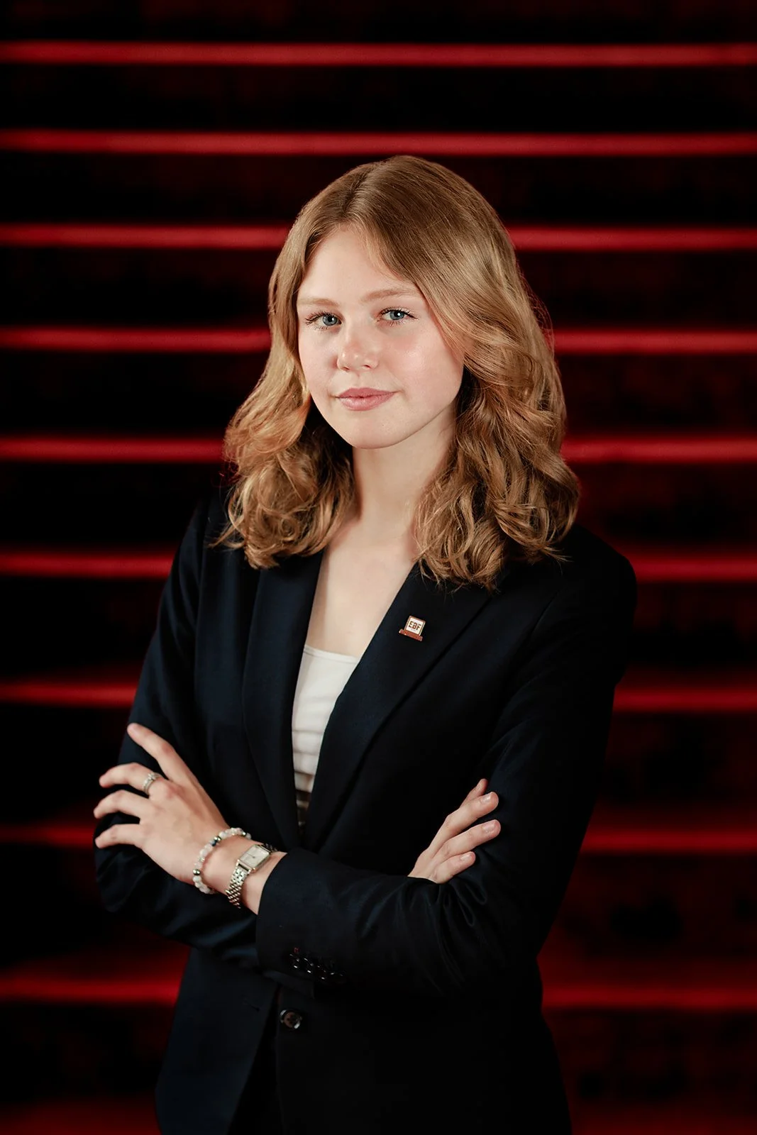 A headshot of a lady with red stripes in the background and a blue blazer 