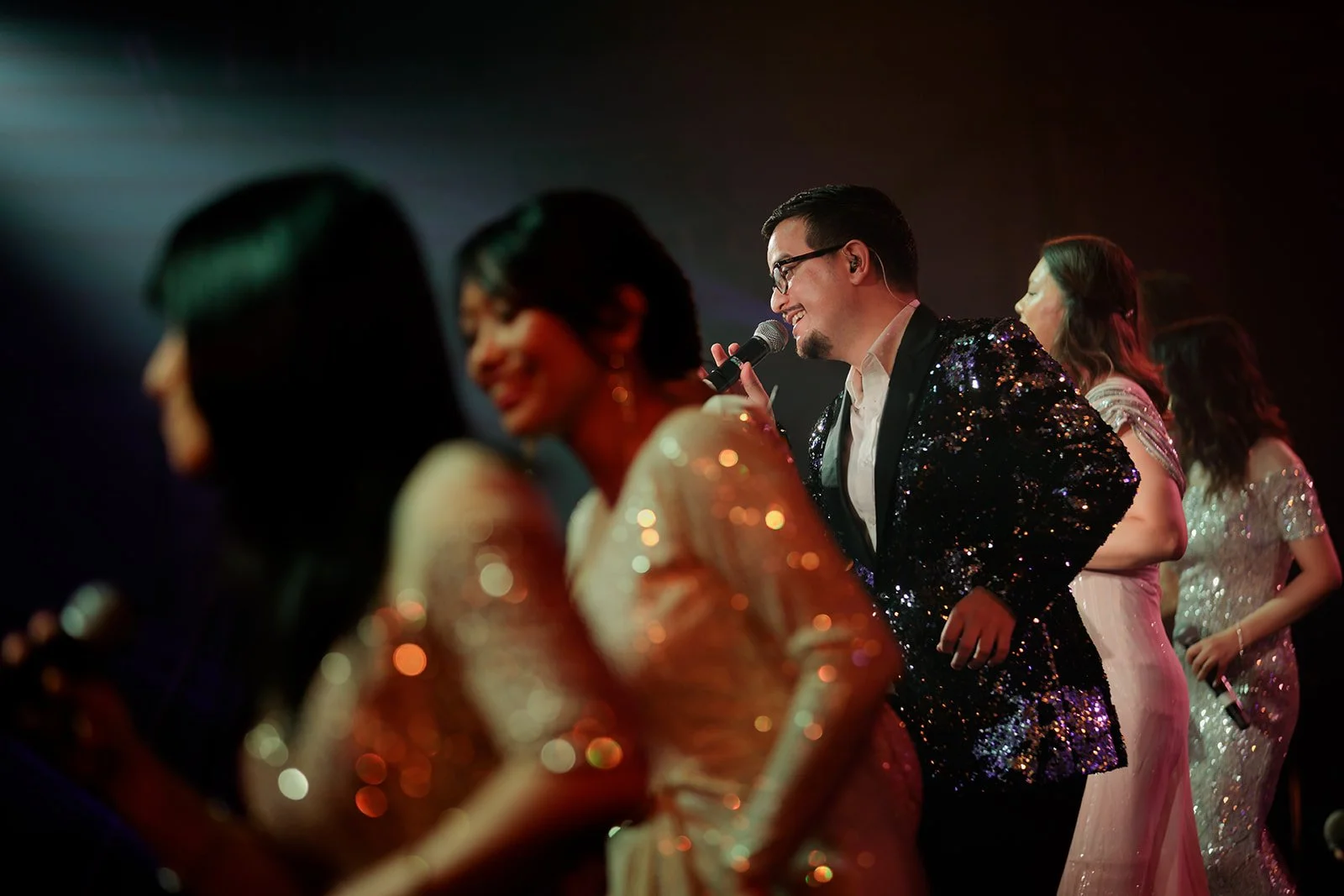 A photograph of a few singers at an event with the main singer being focused on and lit up 