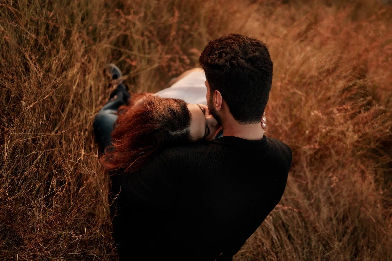 A photograph of a lady with red hair lightly kissing her partners neck, photographed by darius on a couple photography session