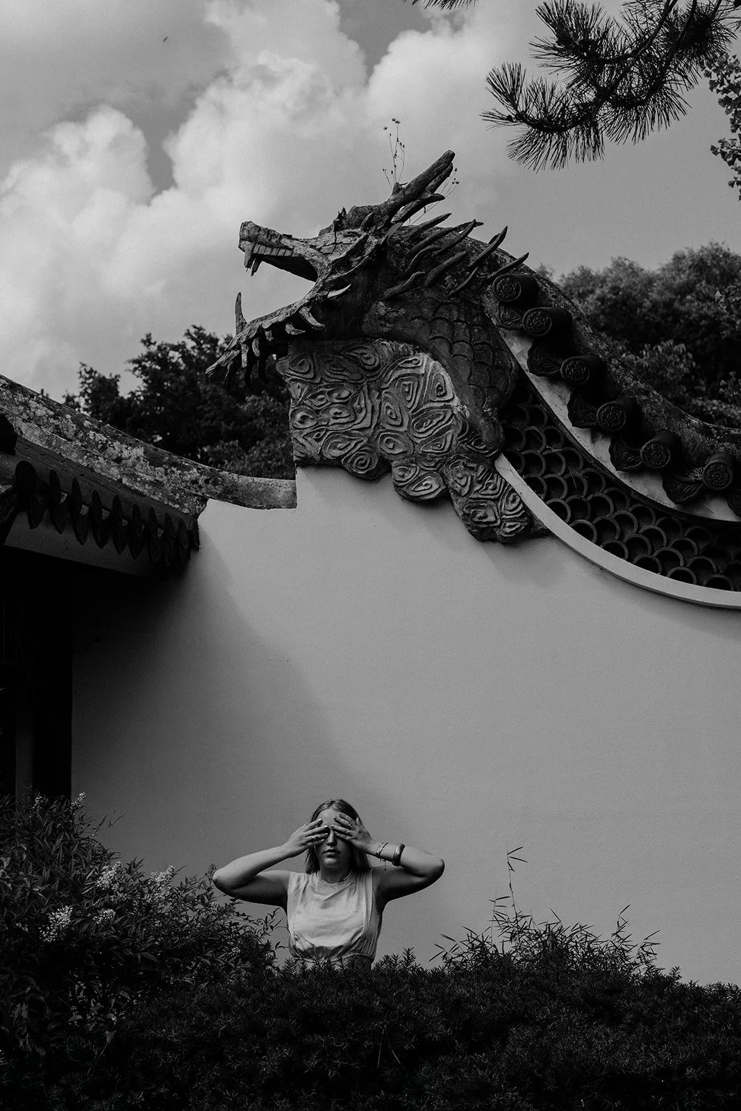 A portrait of a lady closing her eyes facing the camera with old asian architecture in the background