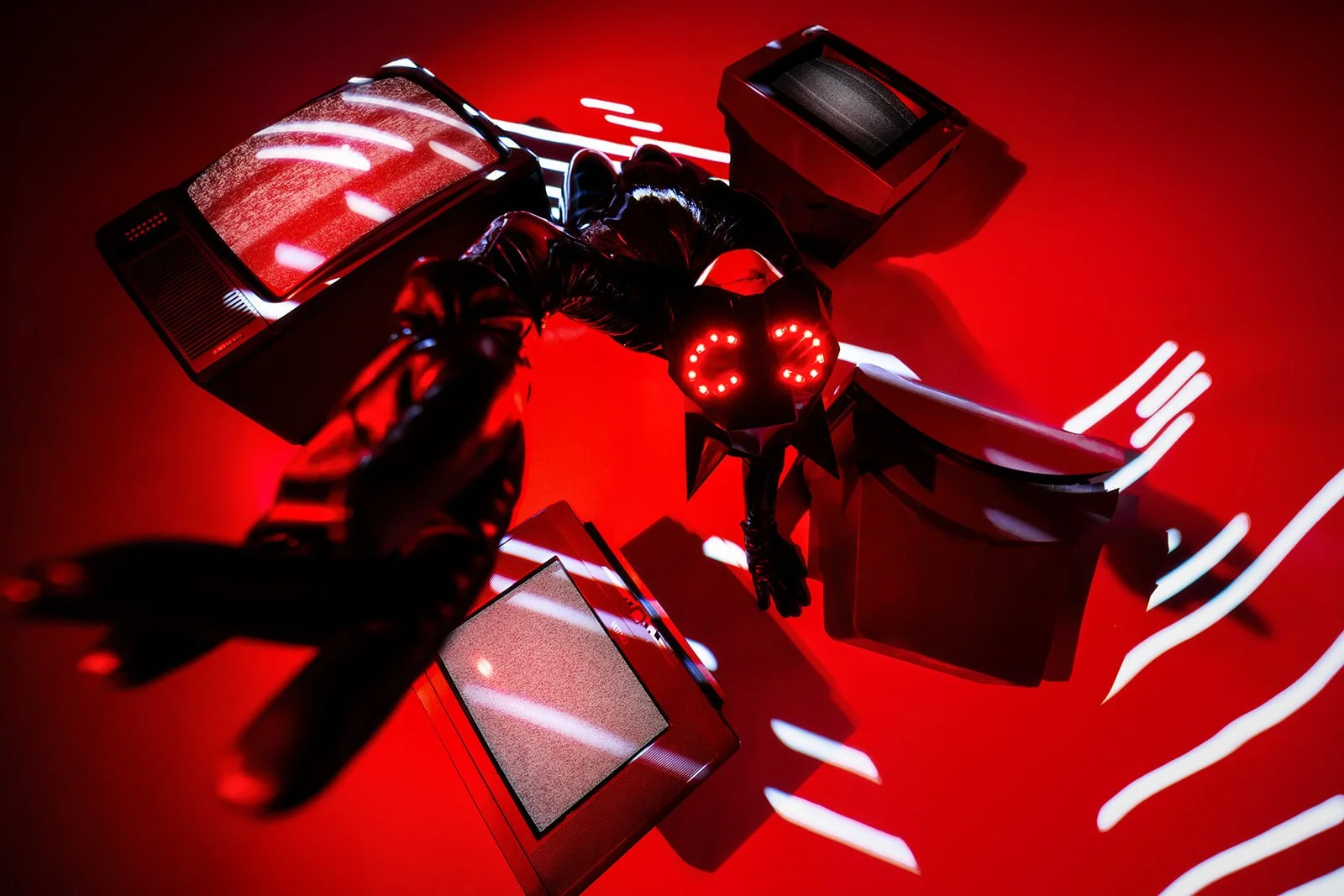 A creative  studio portrait of a lady with a mask sitting around a couple of old tvs and stretching her hand out towards the lens