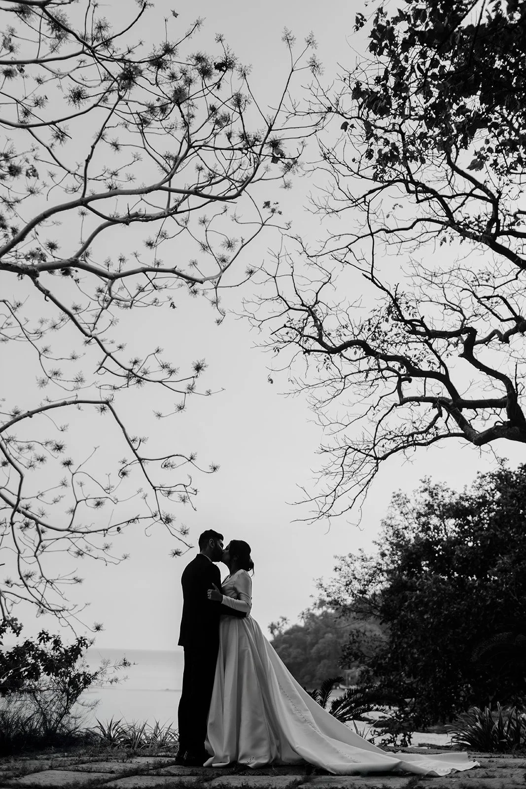 A black and white picture of the bride and groom kissing with the sea in the background taken by Darius N Fernandes 