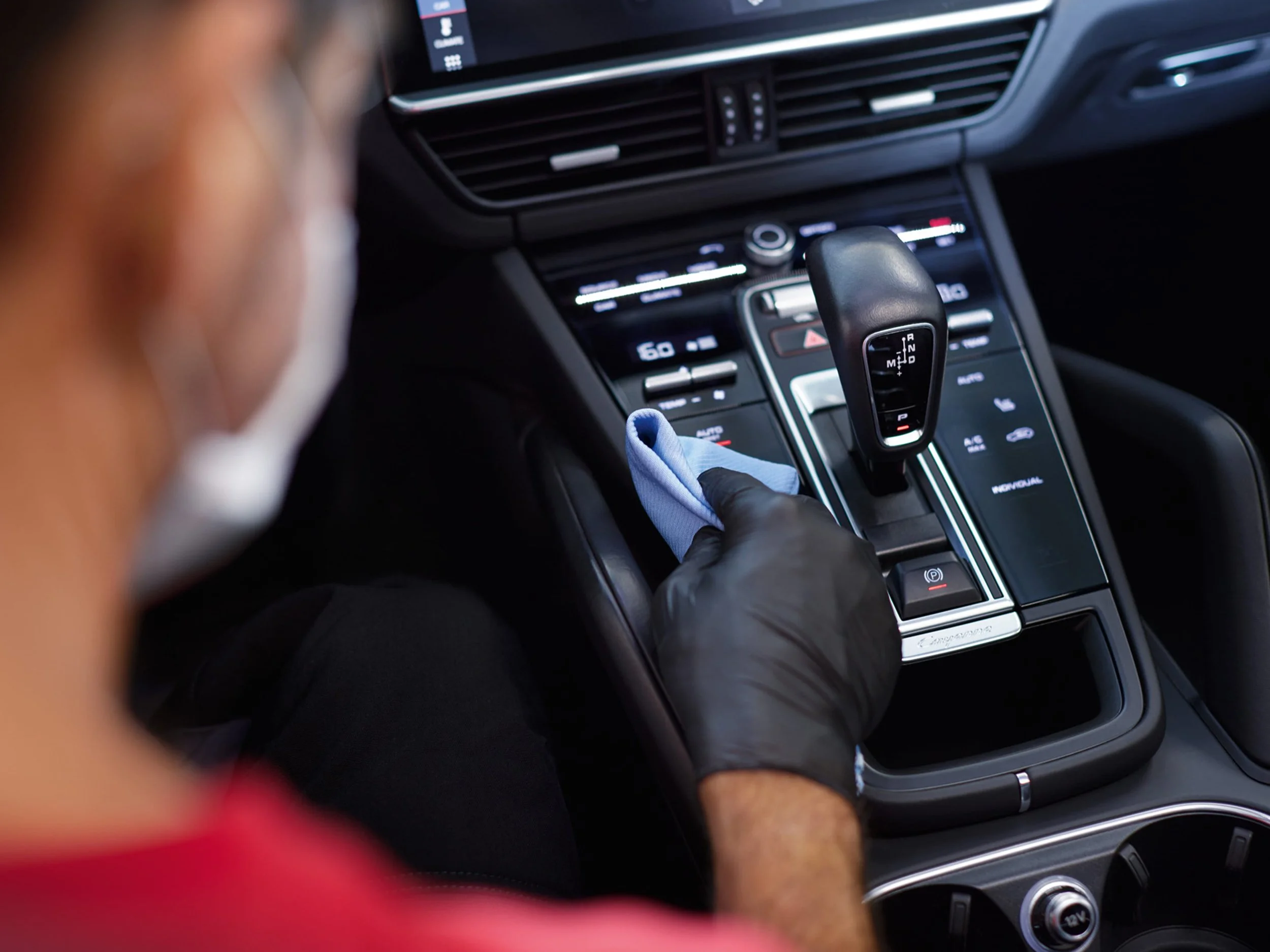 Close-up view of a car's center console featuring a gear shift, climate control buttons, and a digital display, with a person's hand possibly wearing a black glove near the gear shift. interior detailing center console deep clean Toronto