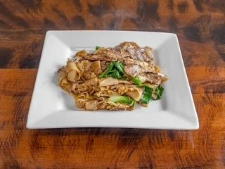 Fettuccine pasta with beef and green vegetables served on a white square plate.