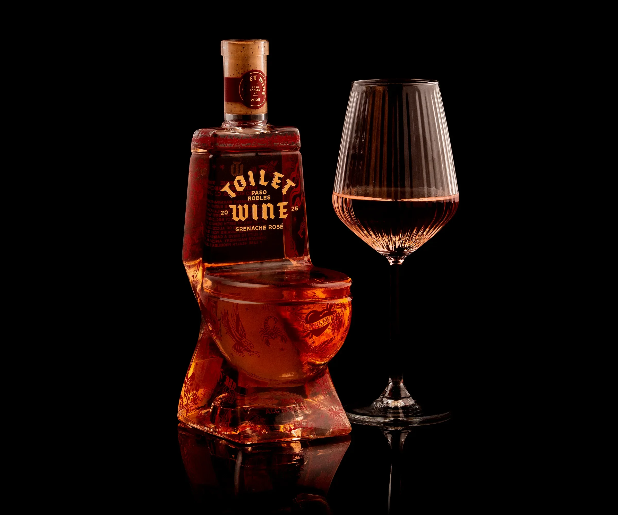 Toilet Wine 2025 Paso Robles Grenache Rosé in a sculptural toilet-shaped glass bottle, displayed beside a glass of rosé against a black background.