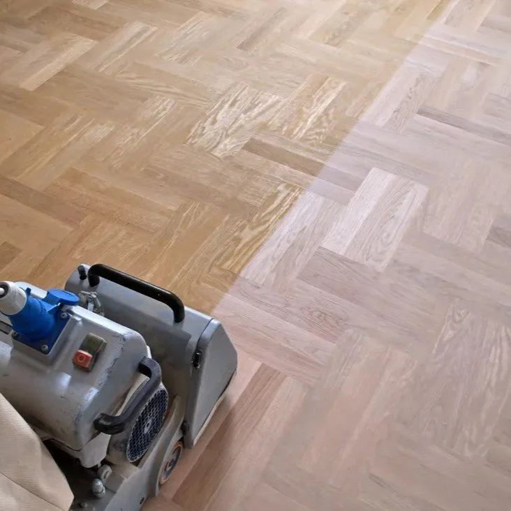 A professional floor sander on a wooden parquet floor, with part of the floor sanded down in preparation for refinishing.