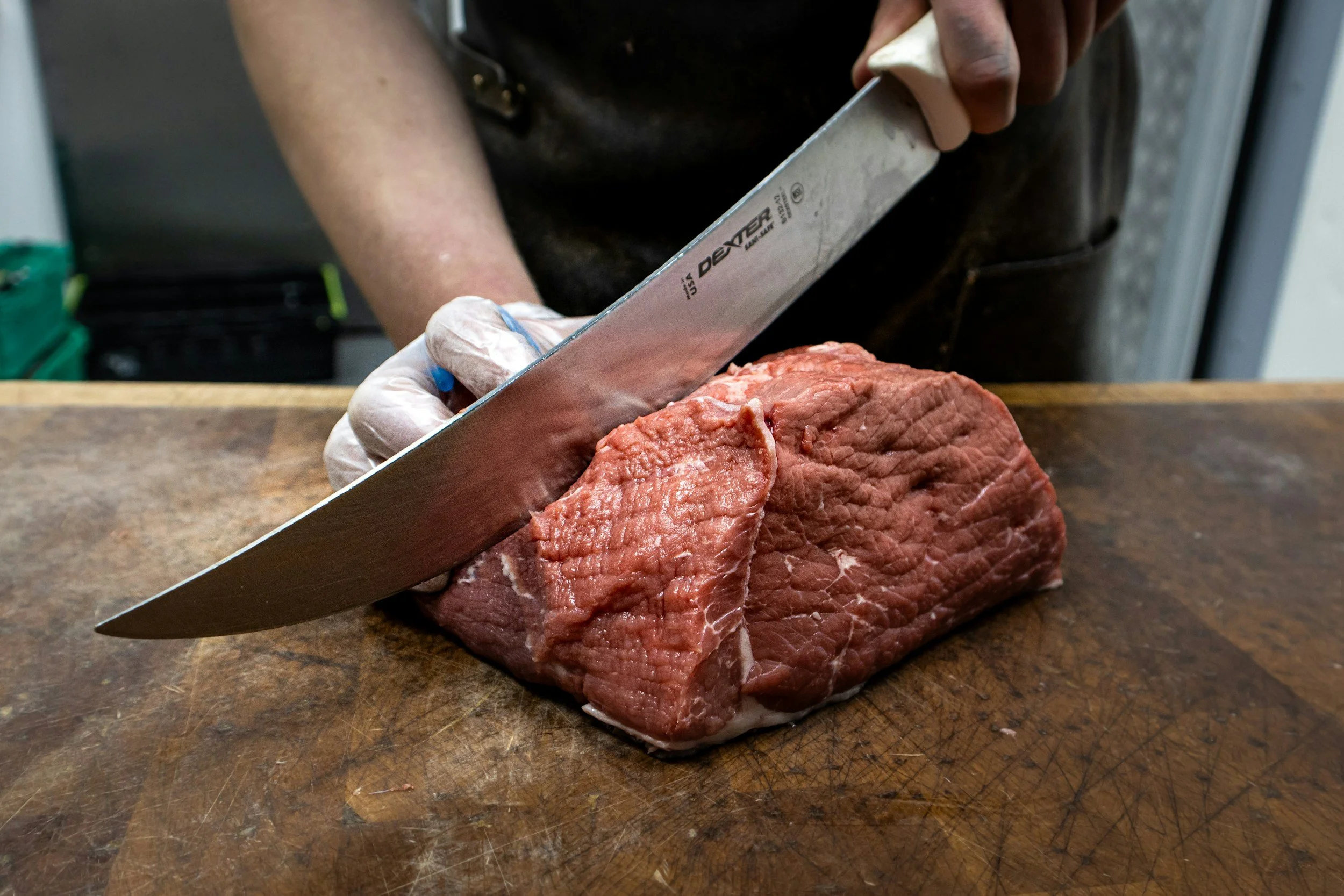 Person slicing a large piece of raw beef on a wooden cutting board.