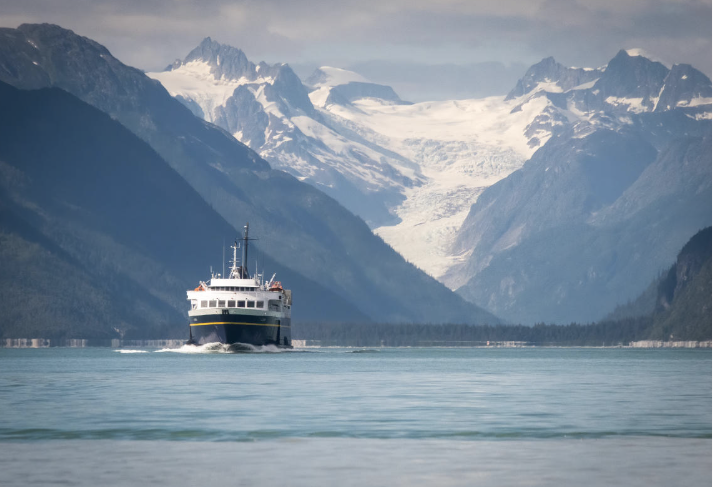 A boat sailing on a fjord with snow-capped mountains in the background.