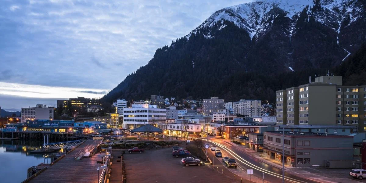 Cityscape at dusk with a waterfront, city buildings, and a mountain in the background. Juneau, Alaska.