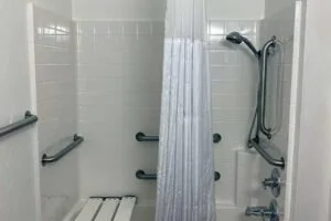 Accessible shower with a showerhead, grab bars, a shower curtain, and a small bench.