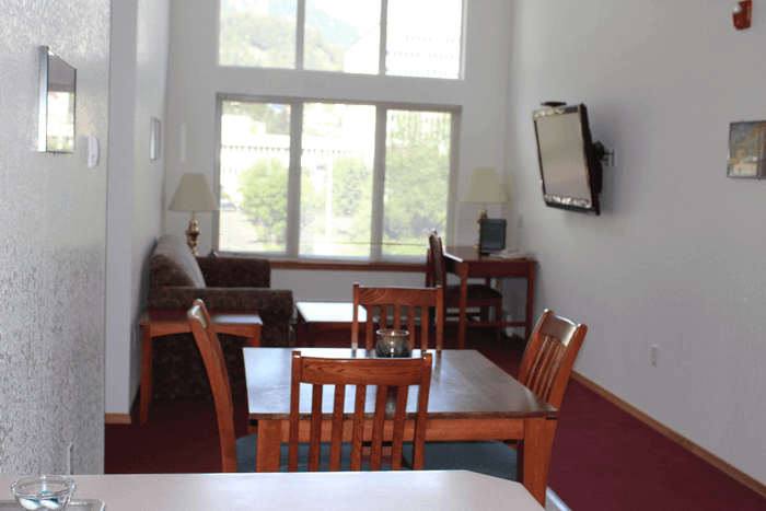 Living room with a dining table and chairs, a sofa near a window, with lamps and a wall-mounted TV.