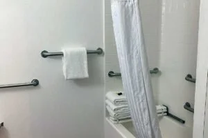 Bathroom with white walls, black grab bars, a wall-mounted towel rack with a white towel, and a shower curtain partially drawn.