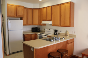 Kitchen with wooden cabinets, white refrigerator, white stove, sink, and beige countertops.