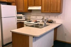 Kitchen with wooden cabinets, white countertops, a refrigerator, a microwave, and a sink.
