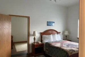 A bedroom with a wooden bed frame, white bedding, two nightstands with lamps, a small picture on the wall, and a mirror reflecting part of the room.