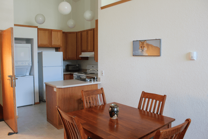 Dining area with wooden table and chairs, kitchen with wood cabinets, refrigerator, stove, microwave, and laundry area with washer and dryer, in a home.