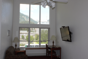 Room with a window showing mountains outside, two lamps on side tables, a wall-mounted TV, and a sofa.