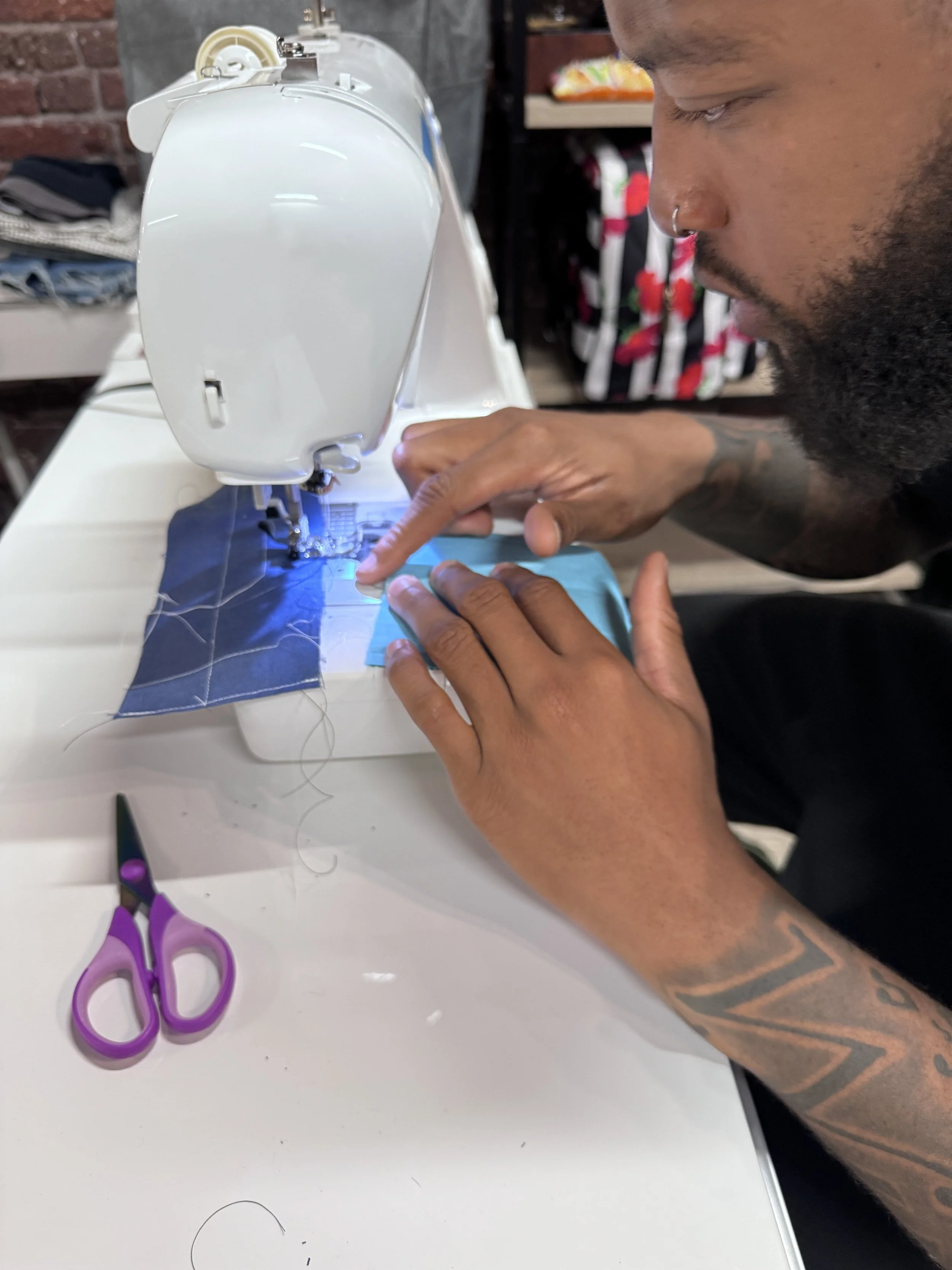 Person sewing fabric with a sewing machine, scissors on white table.