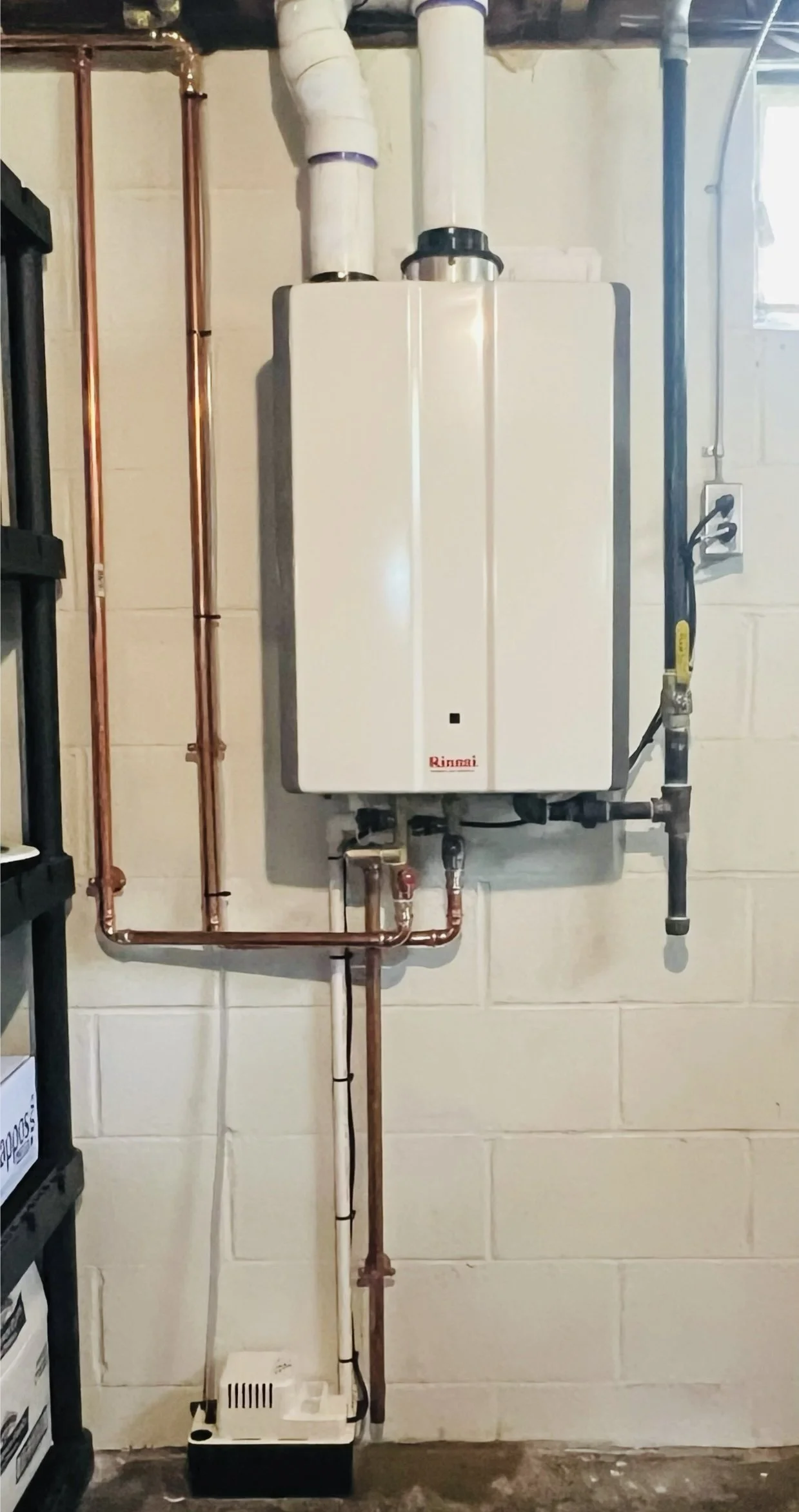 A Rinnai tankless water heater installed on a concrete block wall, with copper and PVC pipes connected for water and gas supply.