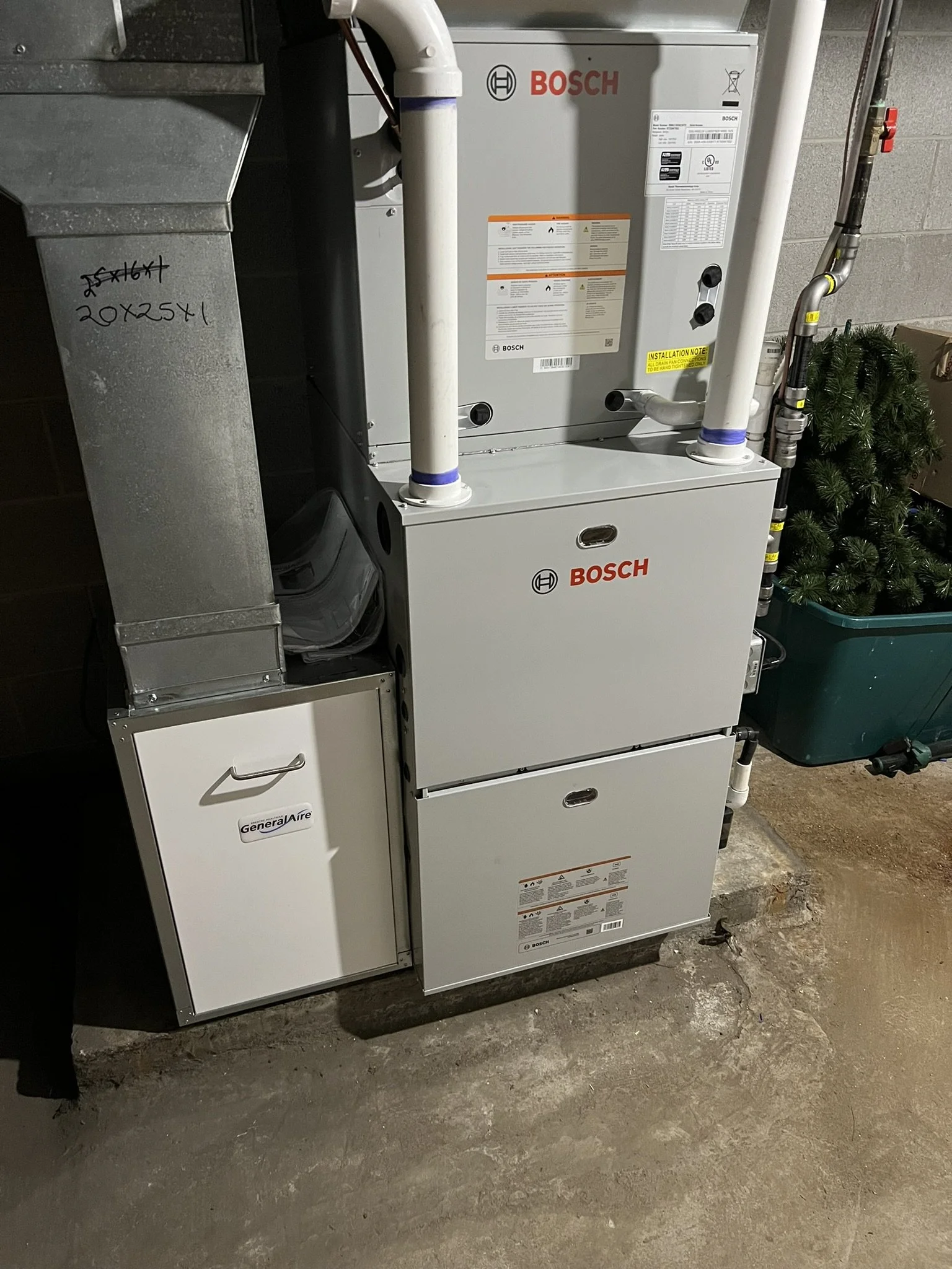 An indoor space with a Bosch HVAC furnace system, pipes, and ducts, a white GeneralAire unit, and a small artificial Christmas tree in a green container.