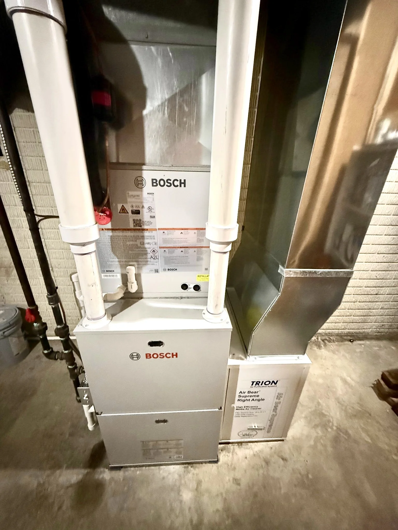 A utility room with a furnace and hot water heater, ductwork, pipes, and electrical wiring, with an unfinished wall and exposed ceiling.