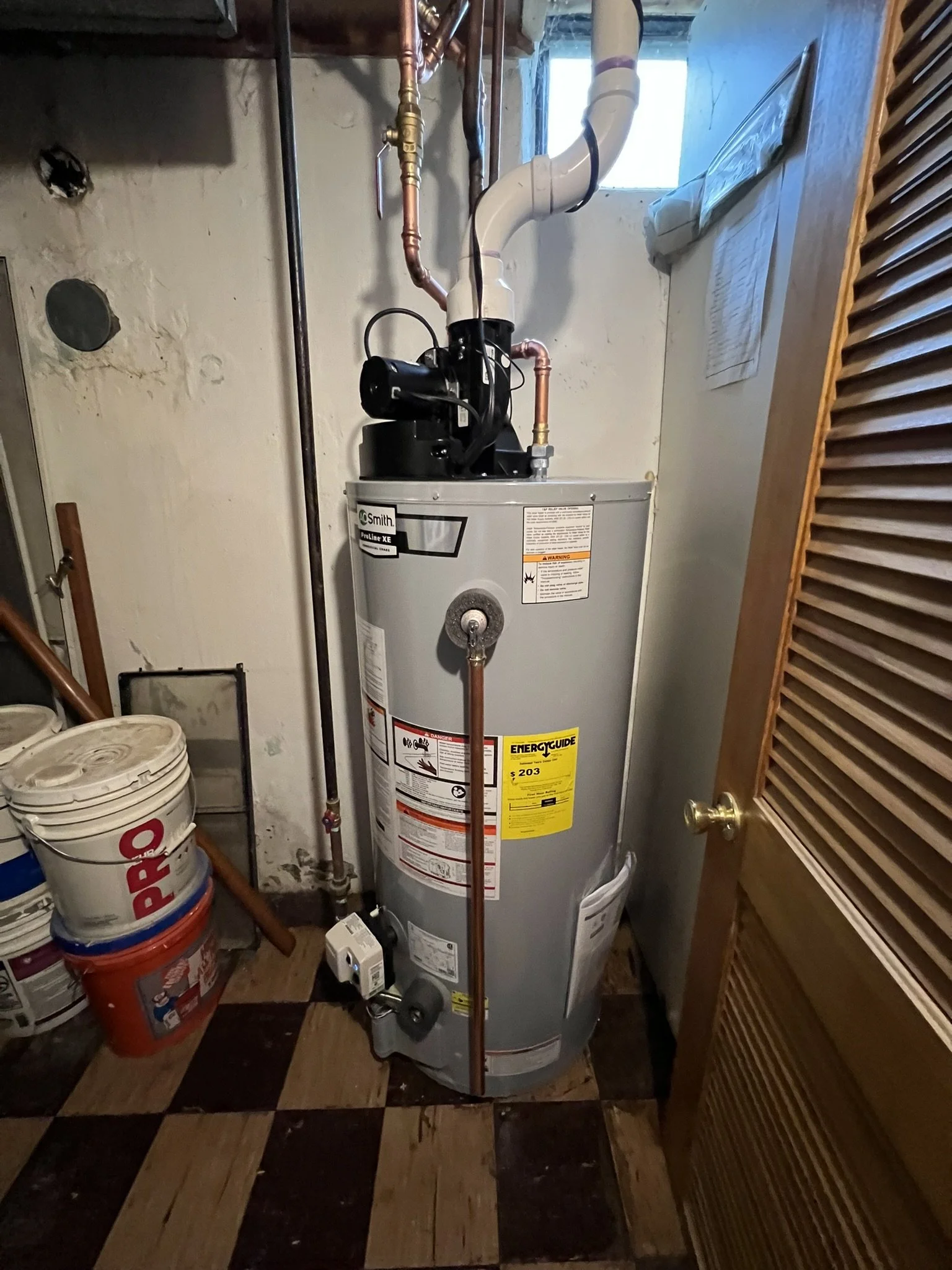 A water heater installed in a utility room with buckets and paint cans nearby.
