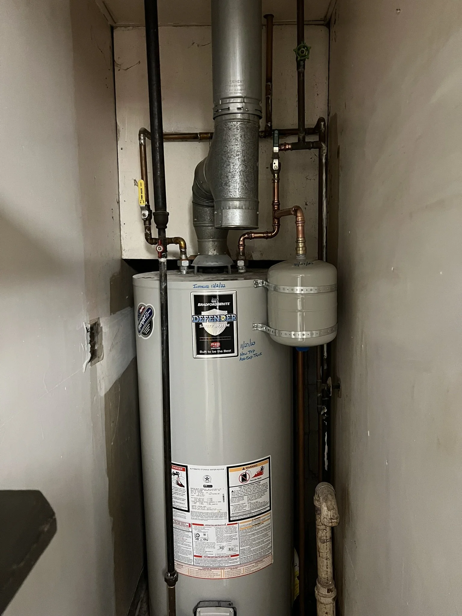 A residential hot water heater installed in a closet with various pipes connected to it.