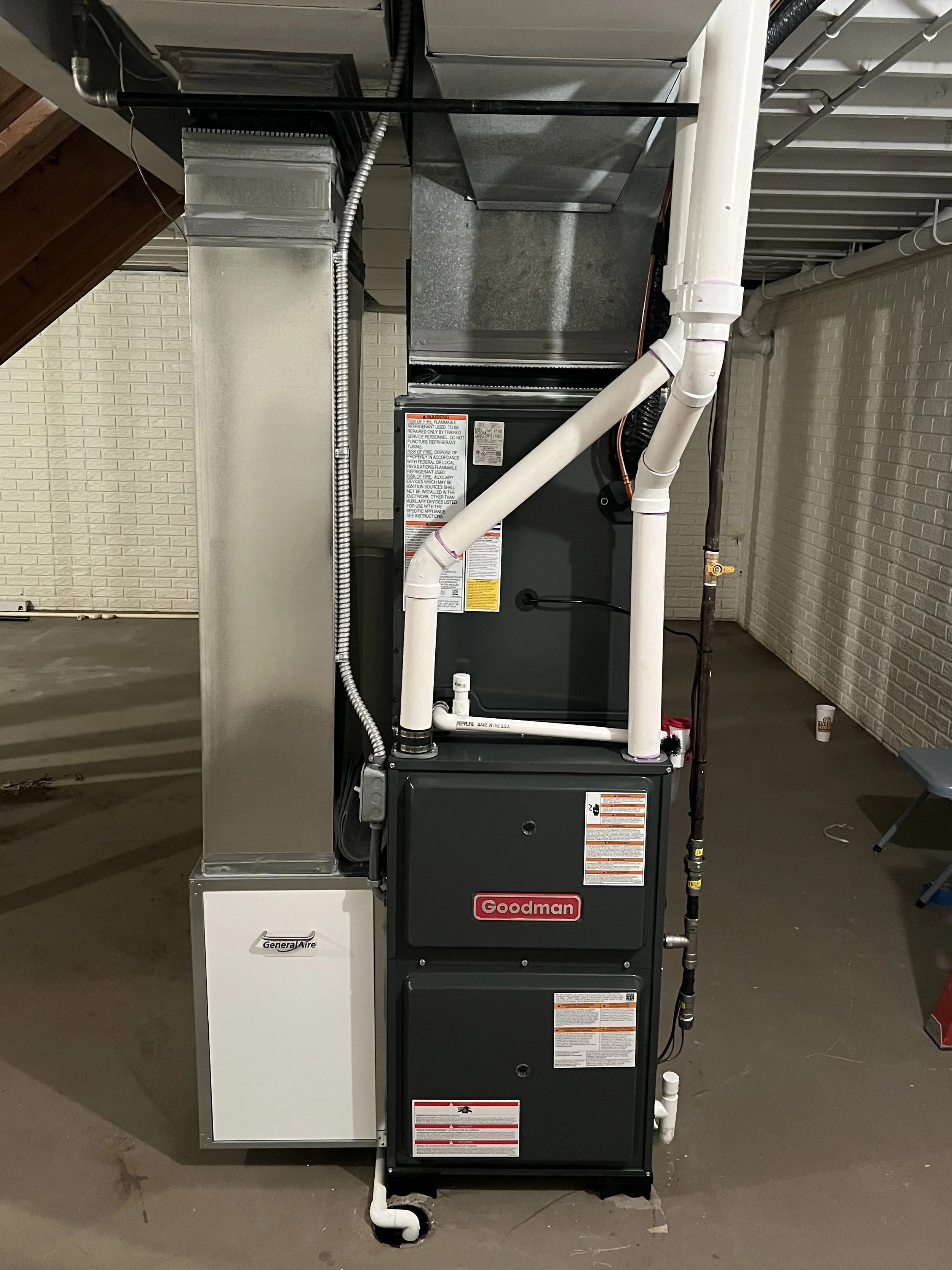 Utility room with HVAC furnace, water heater, and metal ductwork, with exposed wooden framing and a small, exposed bulb light.