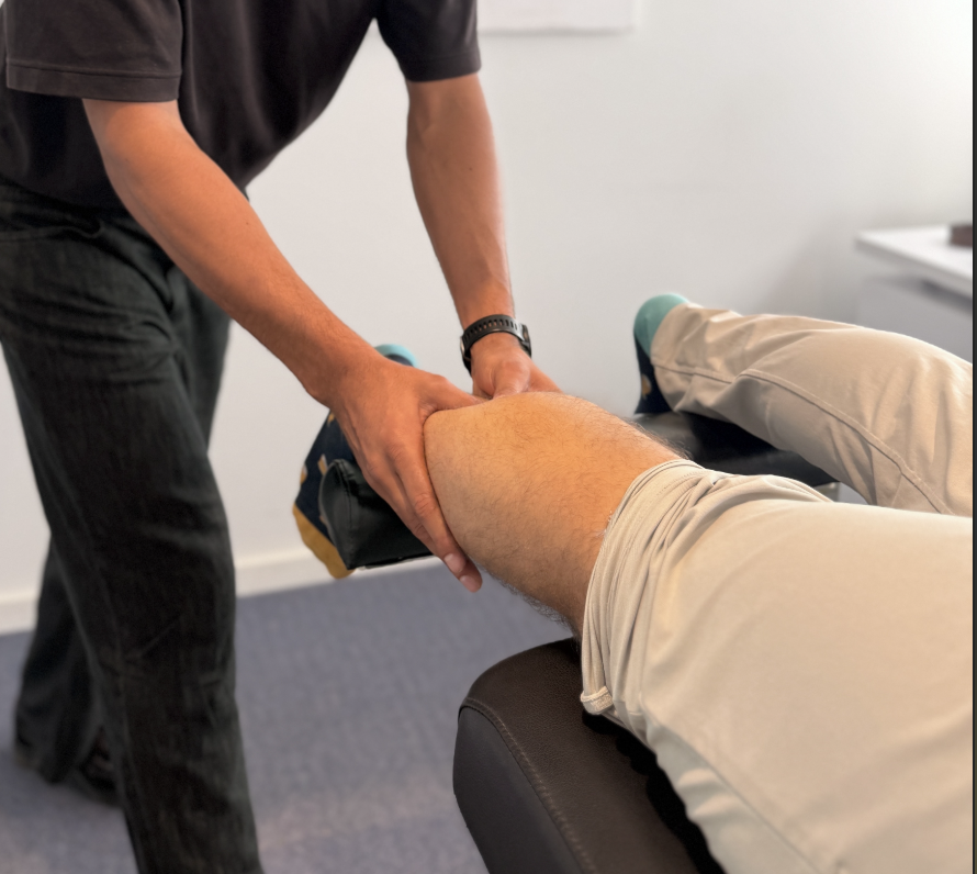 A physical therapist or doctor performing knee therapy or examination on a patient lying on a treatment table.