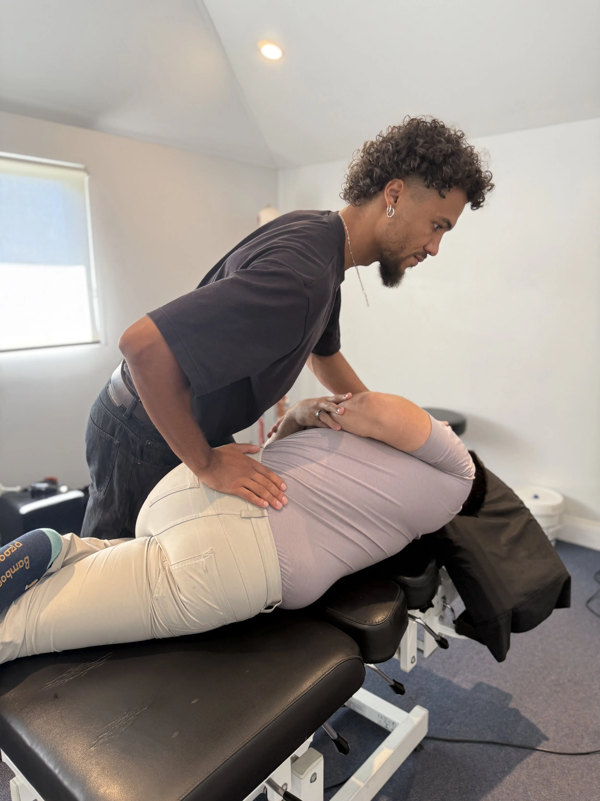 A chiropractor performing an adjustment on a patient lying face down on a chiropractic table in a treatment room.
