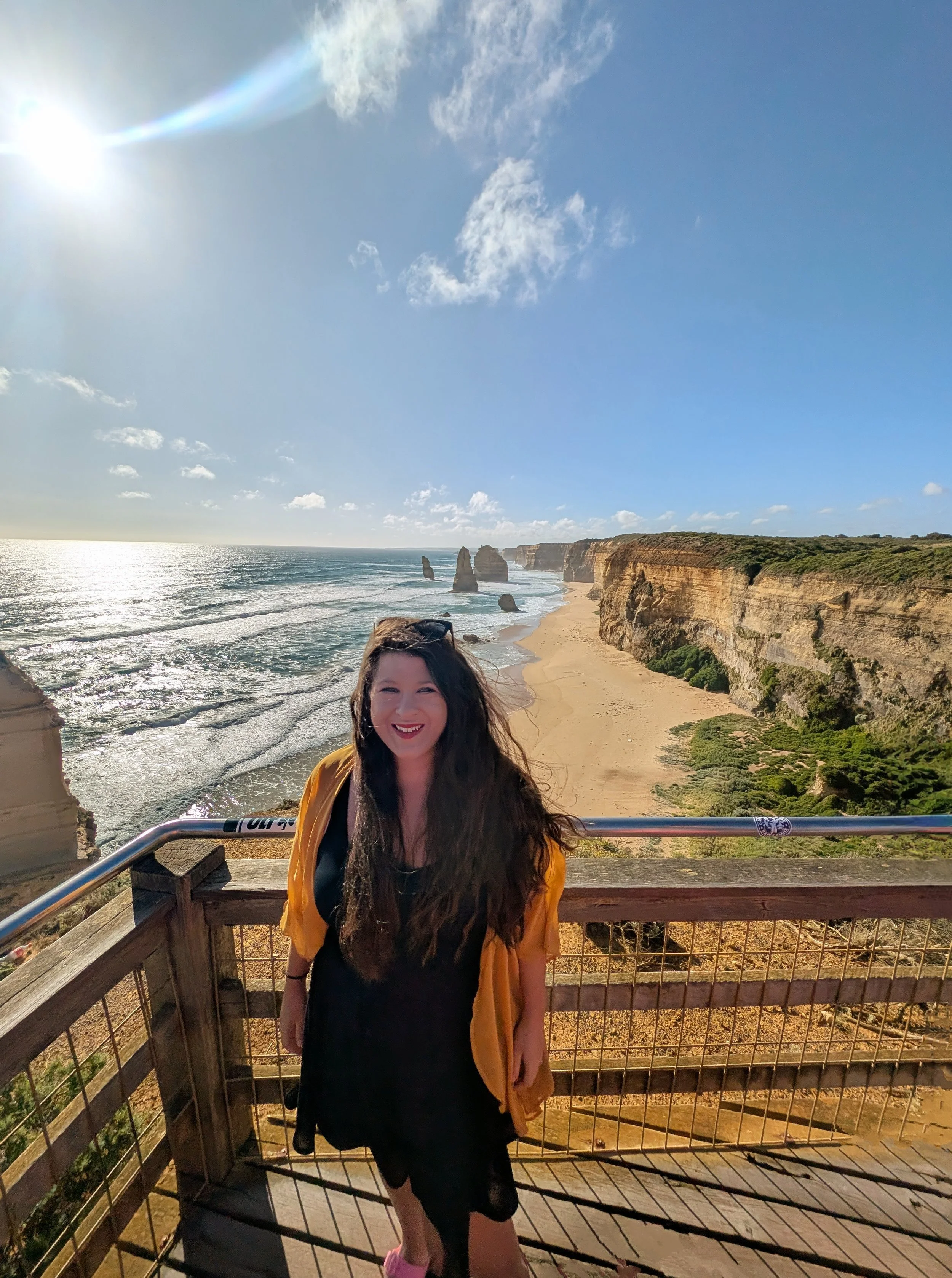 A woman standing on a viewing platform overlooking the coastline of the Twelve Apostles limestone stacks along the Great Ocean Road in Australia.