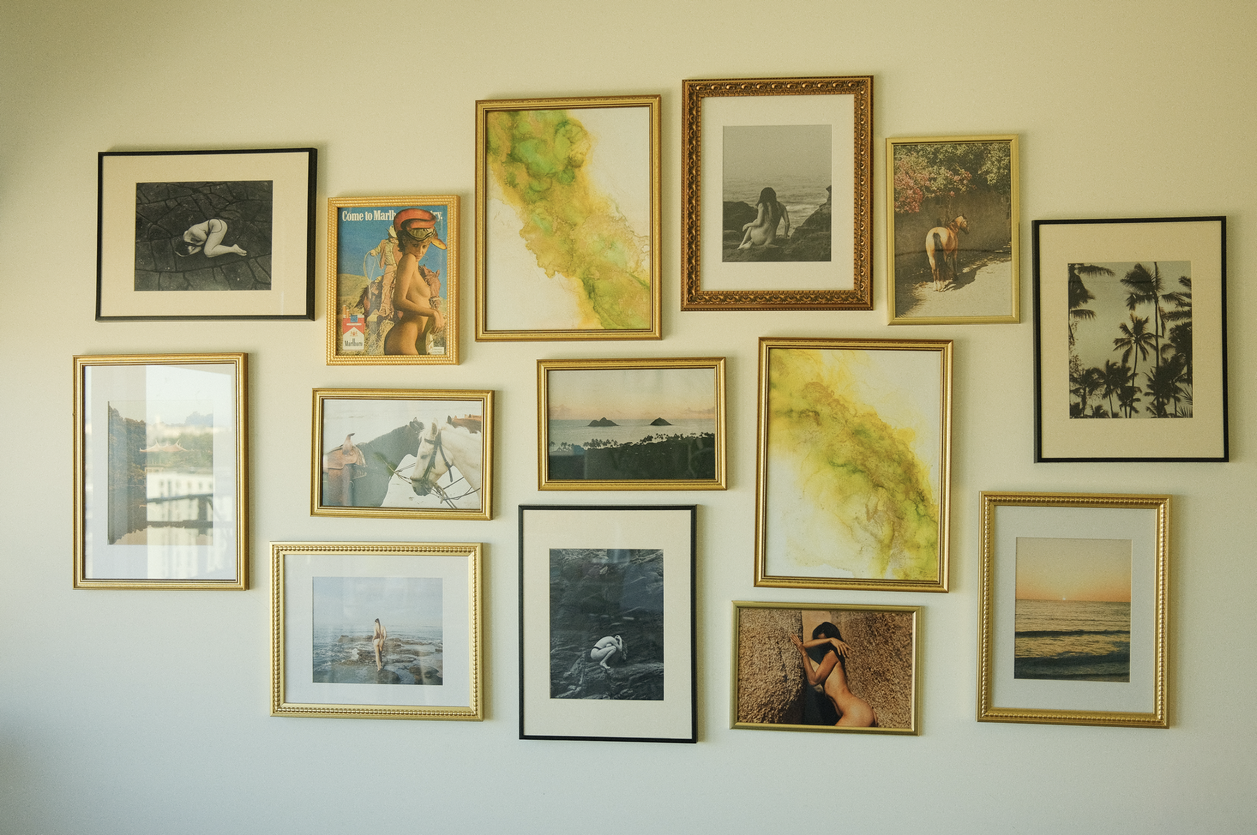 A wall decorated with a collage of framed photographs and artwork, including black and white, color photos, watercolor paintings, and scenic images of nature, beaches, and people.