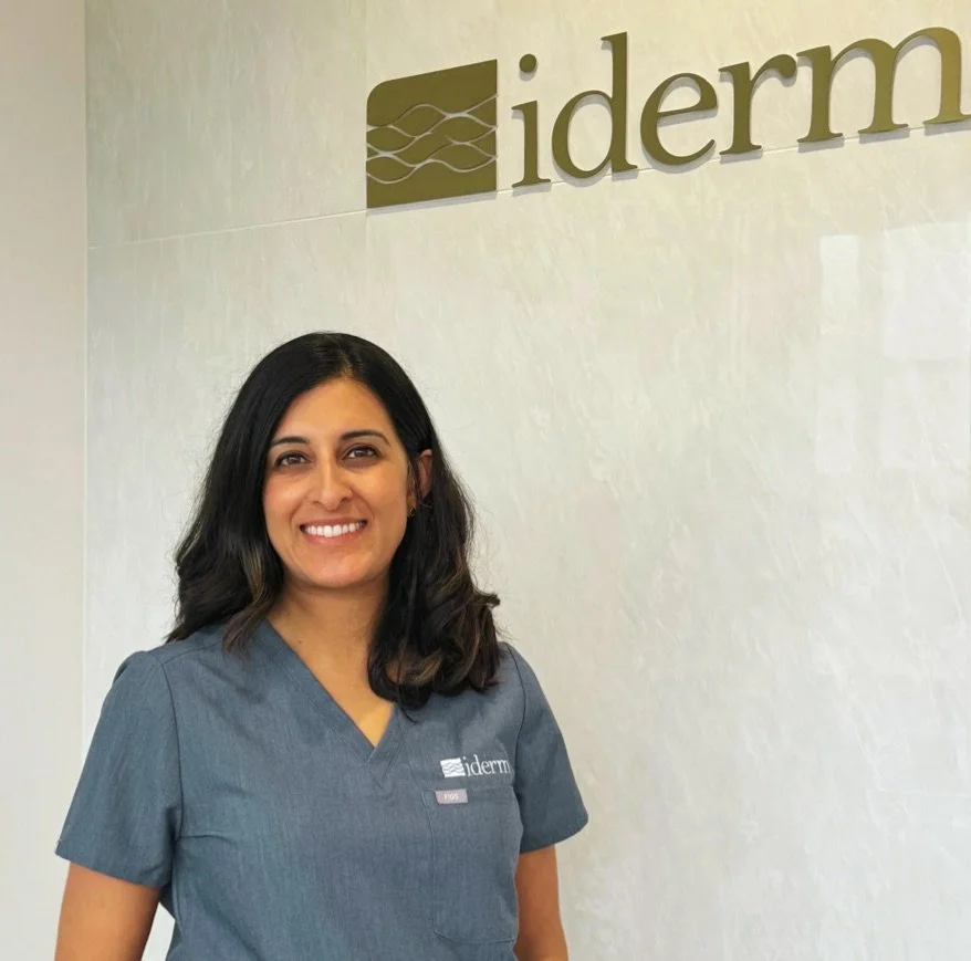 A woman in gray scrubs standing in front of a wall with the 'iderm' logo.