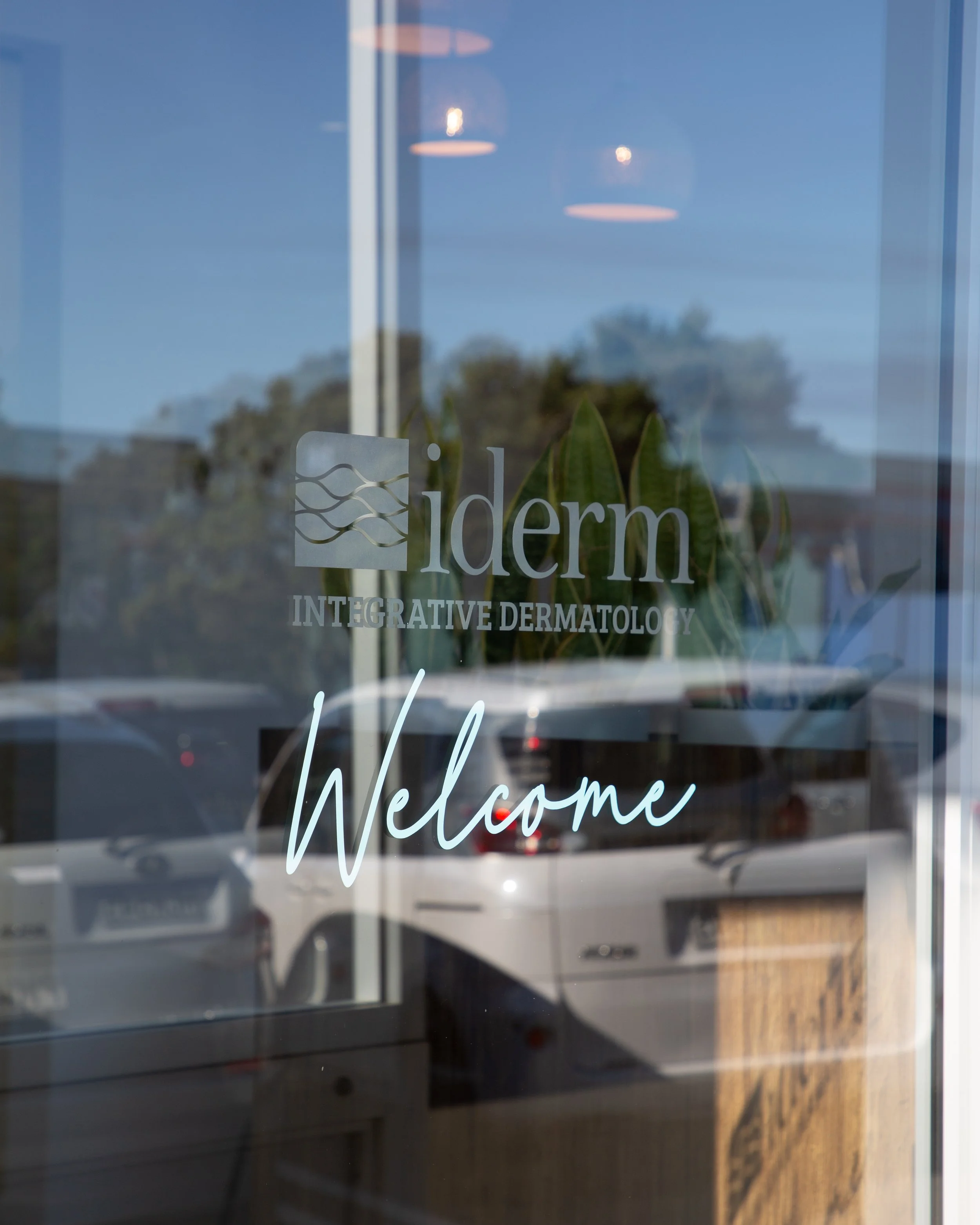 A glass window with the word "Welcome" written in cursive, and the logo of a dermatology clinic with the words "iderm INTEGRATIVE DERMATOLOGY" visible on it.