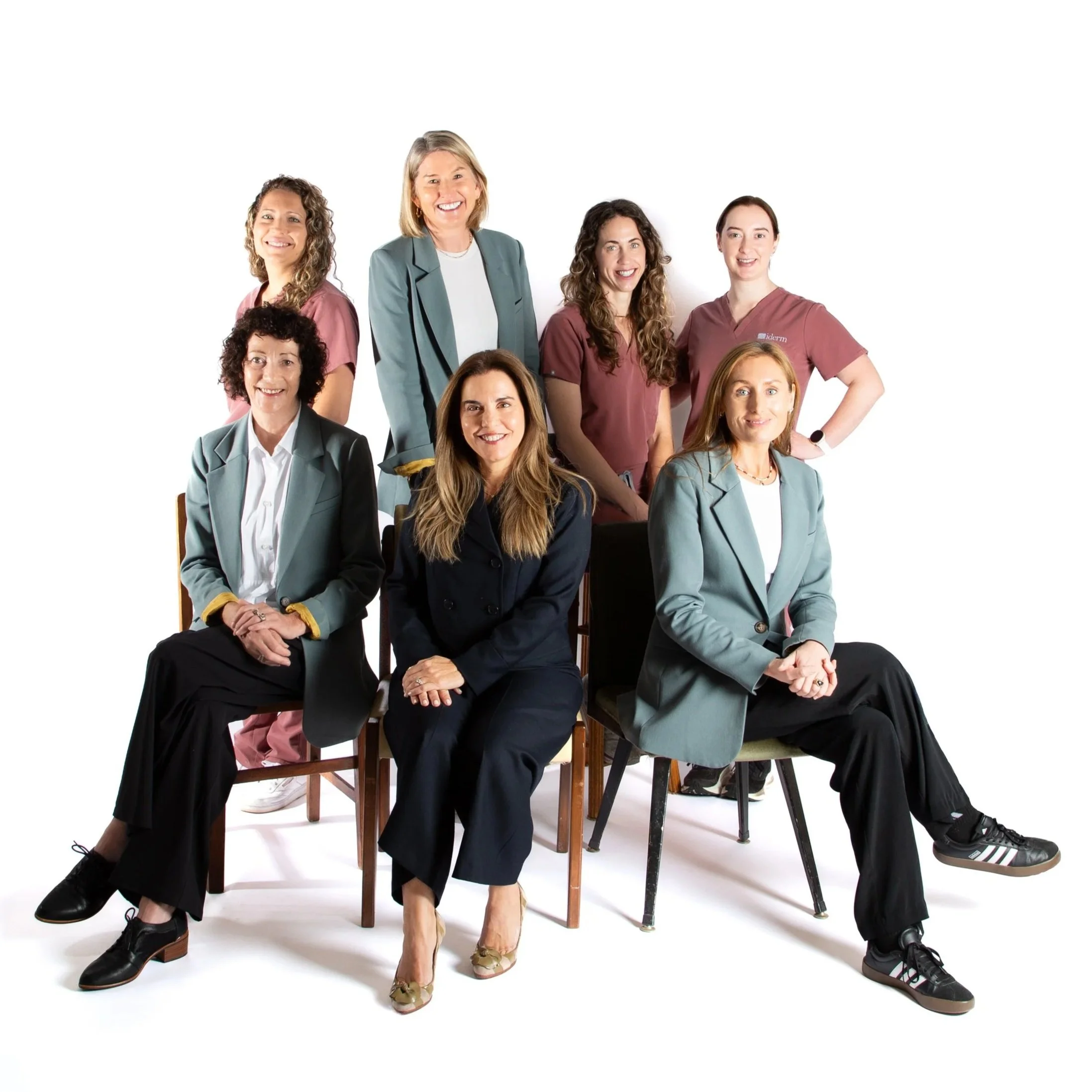 Group of diverse women, some in medical scrubs, sitting and standing against a white background, smiling and posing confidently.