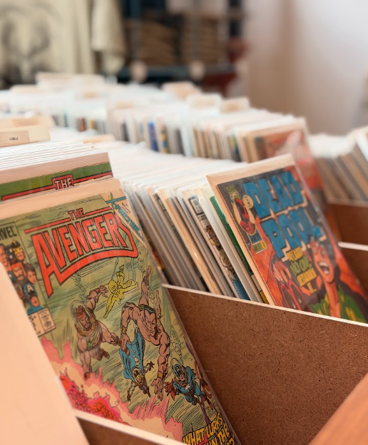 Comics displayed in a store, including Marvel's The Avengers and The Power Pack, arranged in wooden bins.