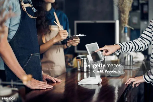 Customer paying at café counter with a tablet POS system, barista taking order in the background.