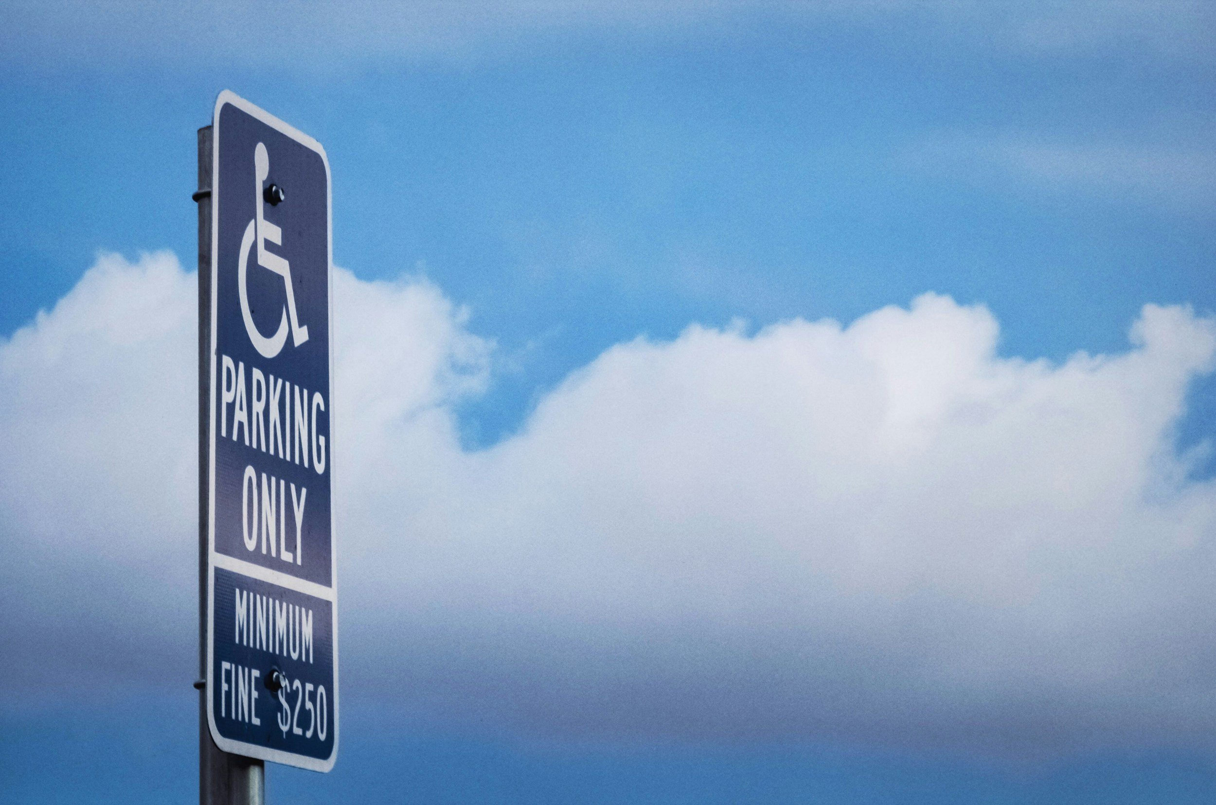 A blue parking sign indicating parking for handicapped with a loading fee of $250, set against a cloudy sky.