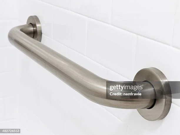 Modern bathroom with a textured gray wall, circular mirror, white vessel sink, black faucet, and a floating shelf with decorative items, illuminated by natural light.