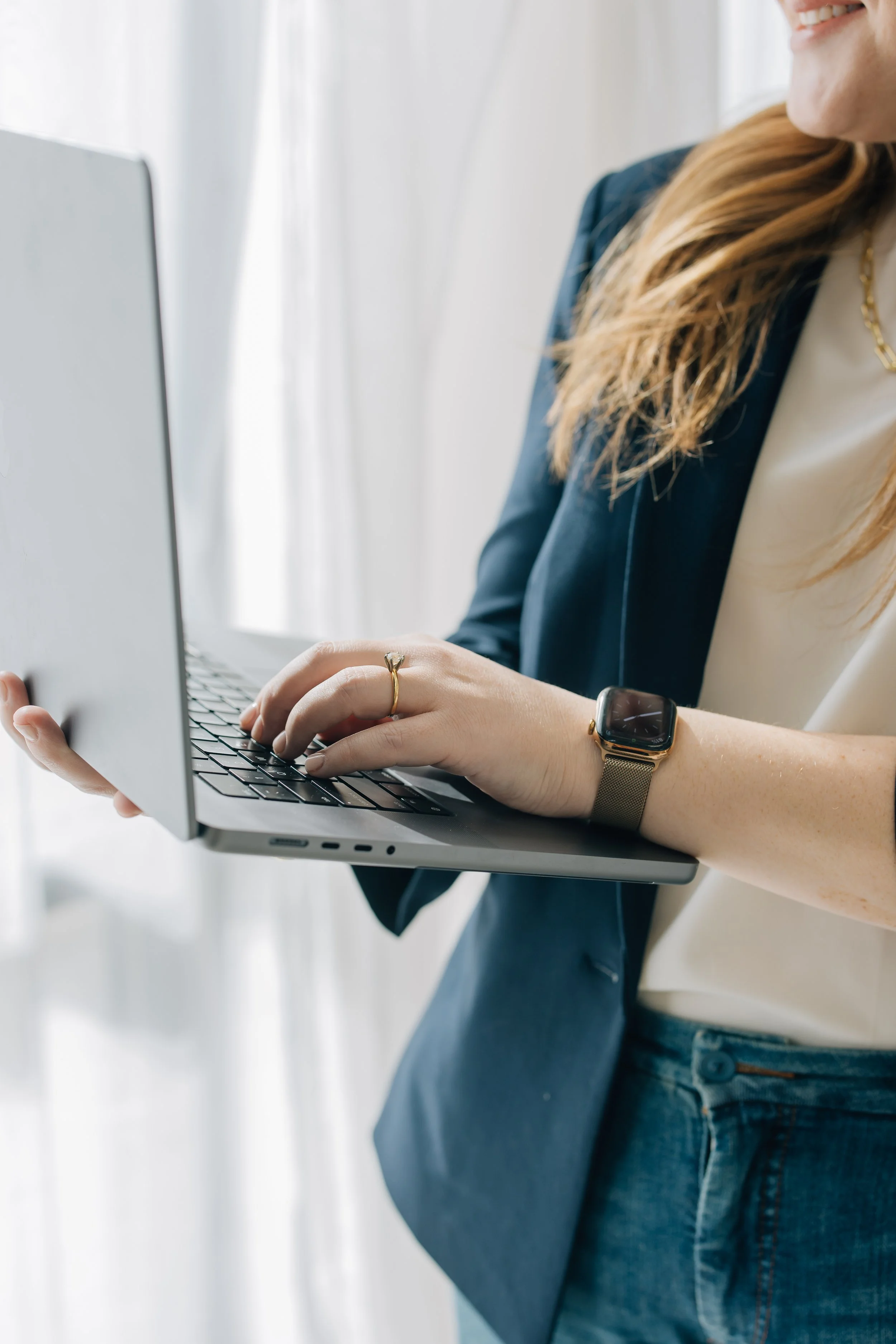 A close up of a woman holding a laptop in one hand while typing on it with the other. You only see the laptop, hands, and part of her torso.