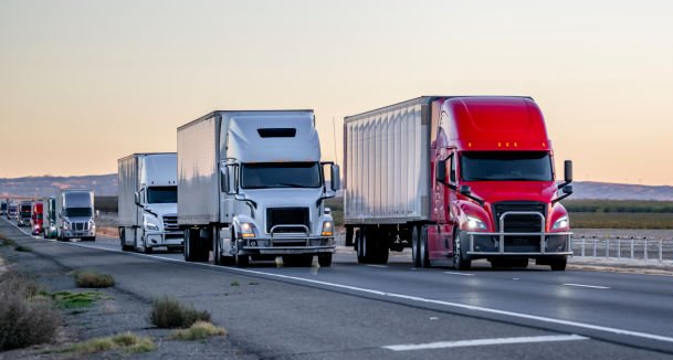 Line of large semi-truck trailers on a highway at sunset