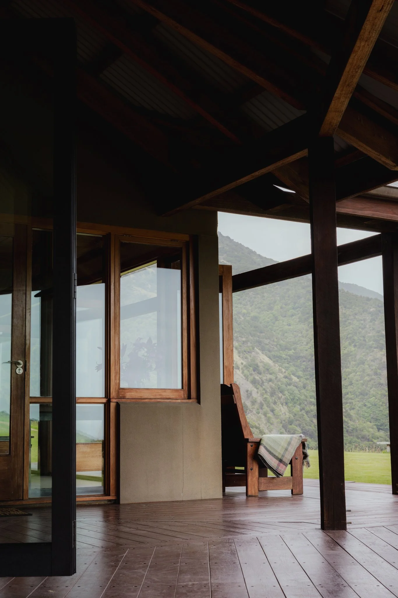 View of a porch area with wooden flooring, open large glass windows, and a scenic mountain landscape in the background.
