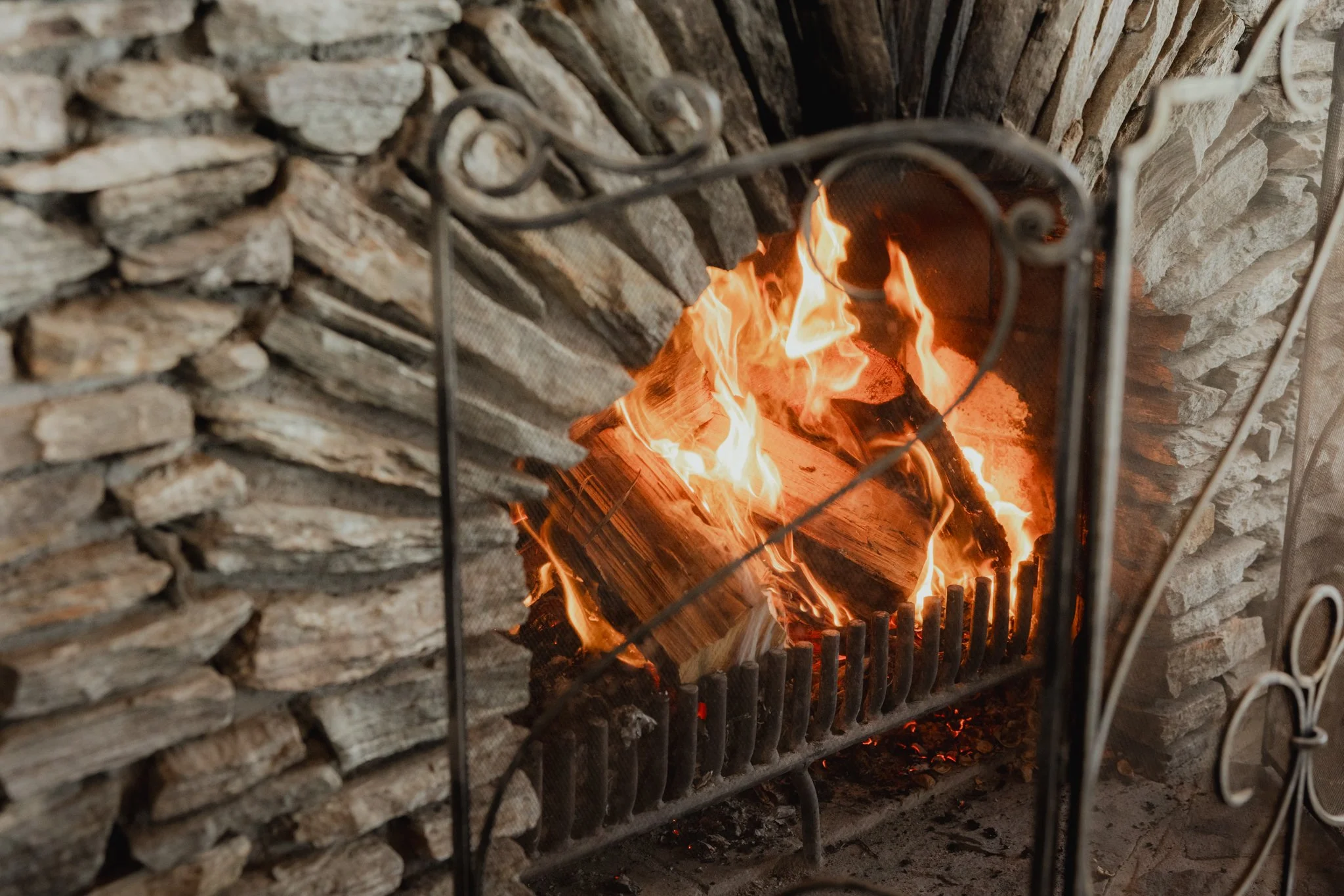 A lit fire inside a stone fireplace with a metal screen in front.