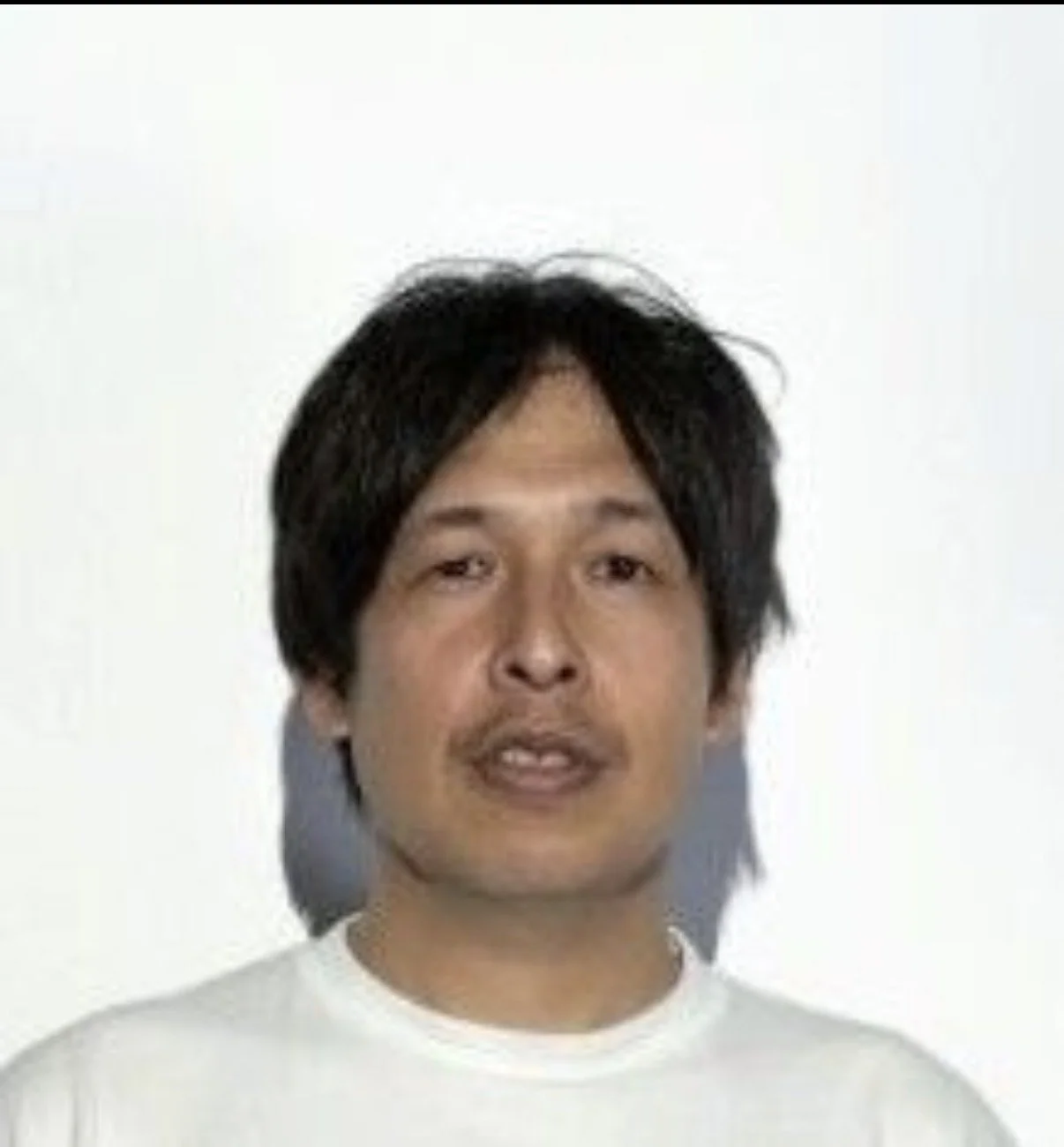 白い背景の前に立つ男性の肖像写真。男性は黒髪で白いシャツを着ている。