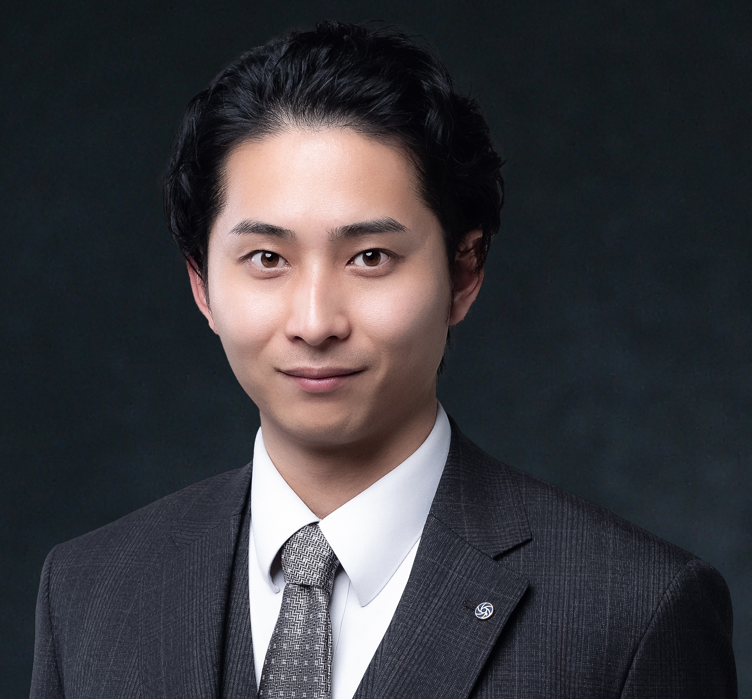 スーツを着た若い男性の顔のアップ。背景は暗い色。