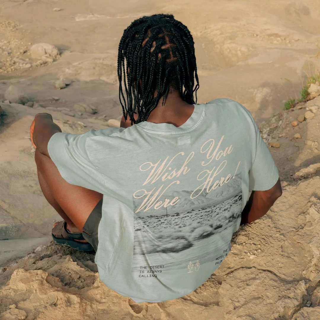 lifestyle mockup of a young person sitting on a rock with their back to the camera, showcasing the custom design on the back of their t-shirt