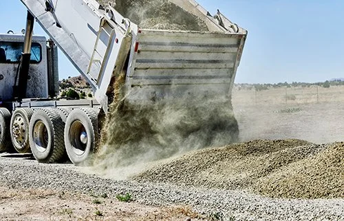 A construction vehicle dumping gravel onto a pile at a construction site.