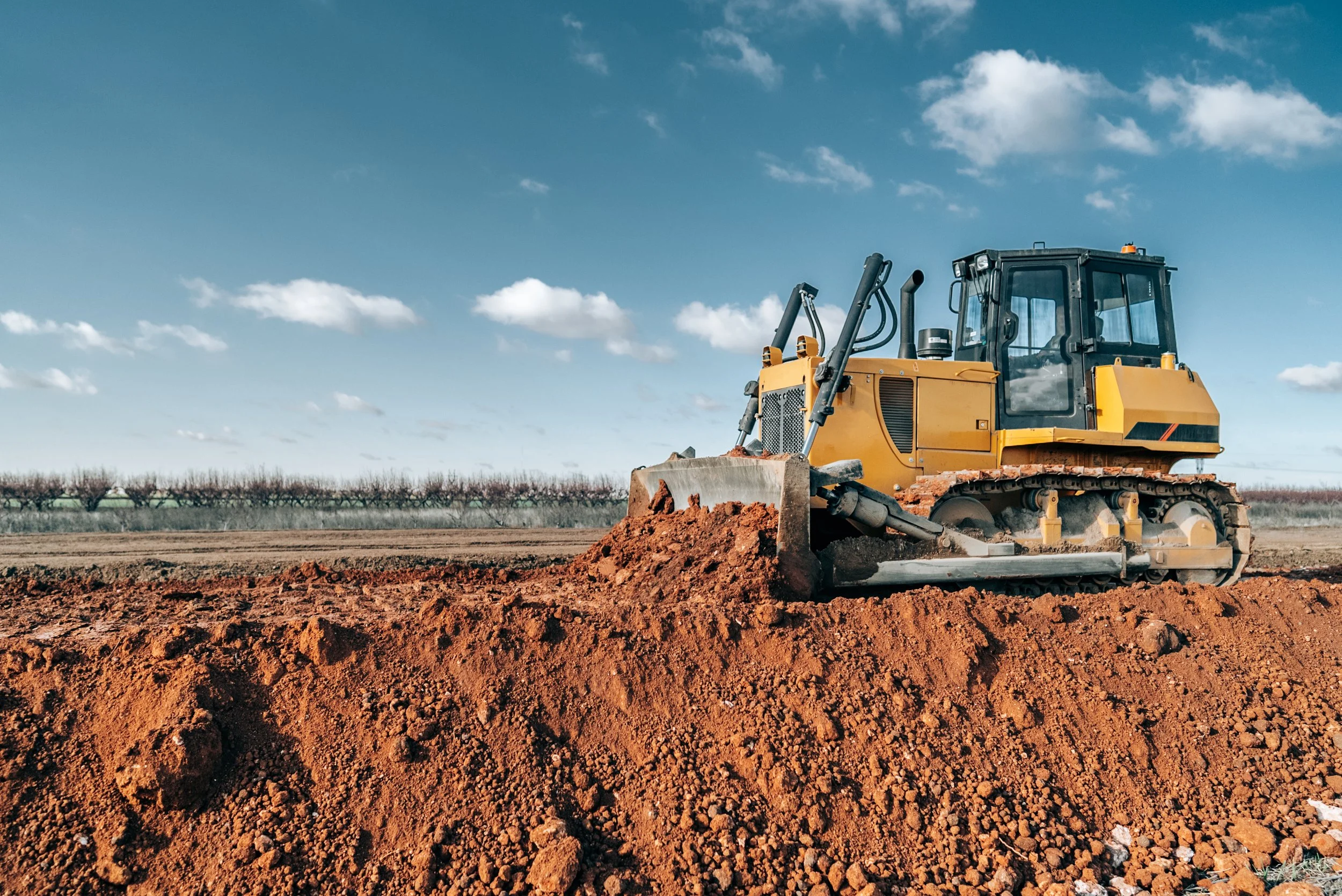 A bulldozer moving soil in a field beneath a partly cloudy sky.