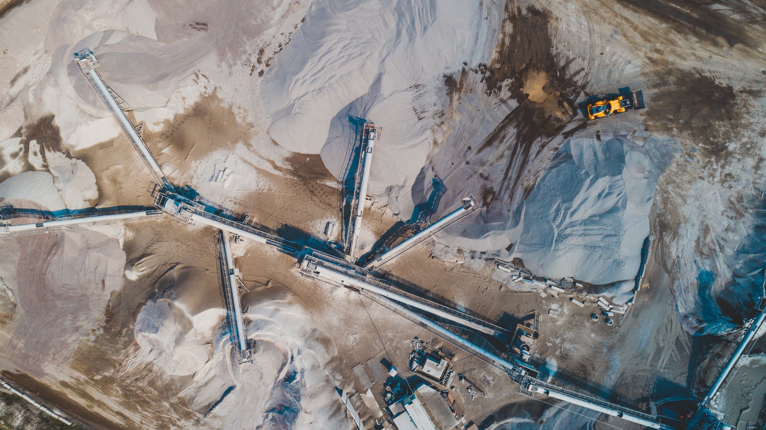 An aerial view of a mining operation with large conveyor belts and trucks in a barren, sandy landscape.